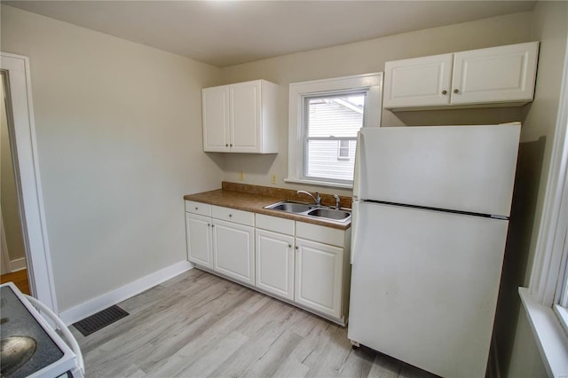 kitchen featuring a sink, white cabinetry, baseboards, light wood-type flooring, and freestanding refrigerator