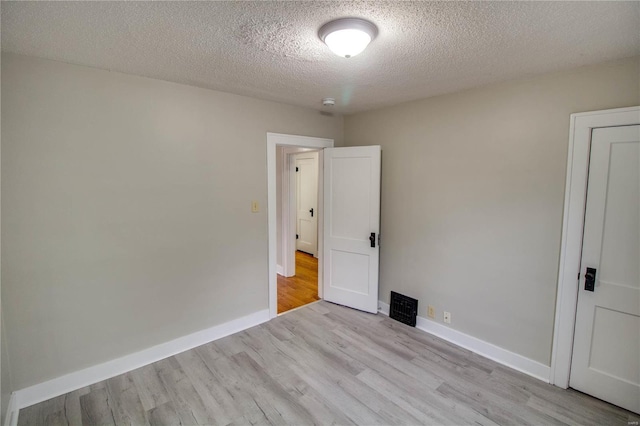 unfurnished room featuring light wood-style floors, a textured ceiling, and baseboards