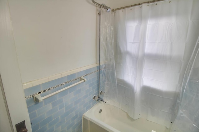 full bathroom with wainscoting, shower / bath combo with shower curtain, and tile walls