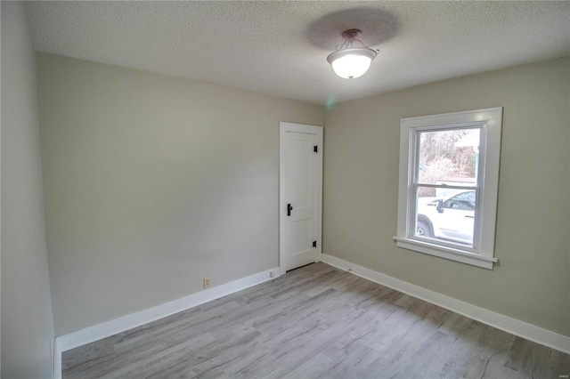 empty room featuring light wood-type flooring, a textured ceiling, and baseboards