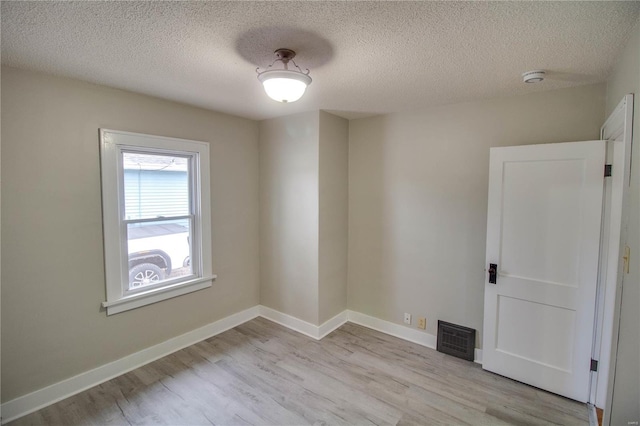 unfurnished room with light wood-type flooring, visible vents, a textured ceiling, and baseboards