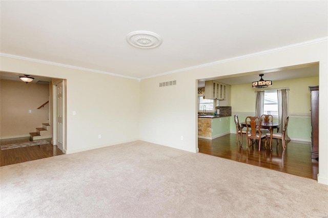 carpeted living room featuring a sink, visible vents, baseboards, stairs, and ornamental molding