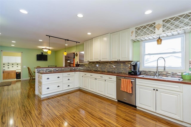 kitchen featuring dishwasher, a peninsula, dark countertops, and a sink