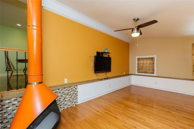 unfurnished living room featuring baseboards, ceiling fan, wood finished floors, vaulted ceiling, and crown molding