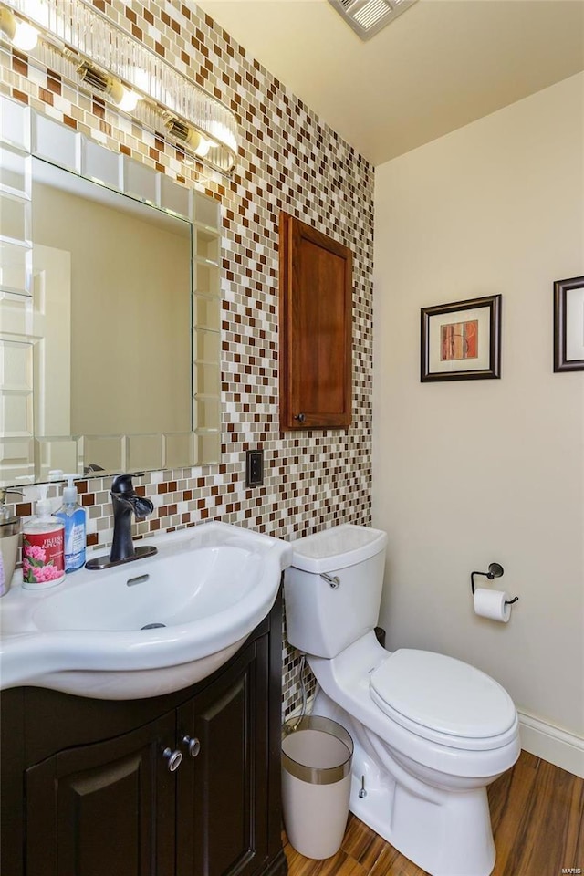 half bath with toilet, wood finished floors, vanity, baseboards, and backsplash