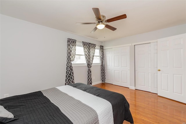 bedroom with ceiling fan, light wood-style floors, baseboards, and multiple closets