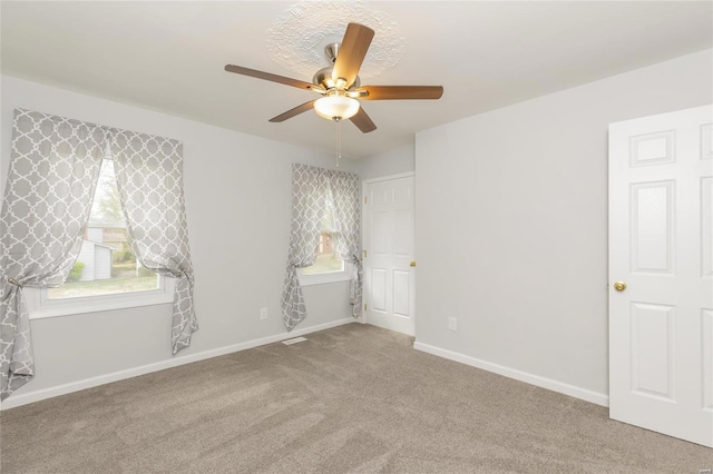 carpeted empty room featuring a ceiling fan and baseboards