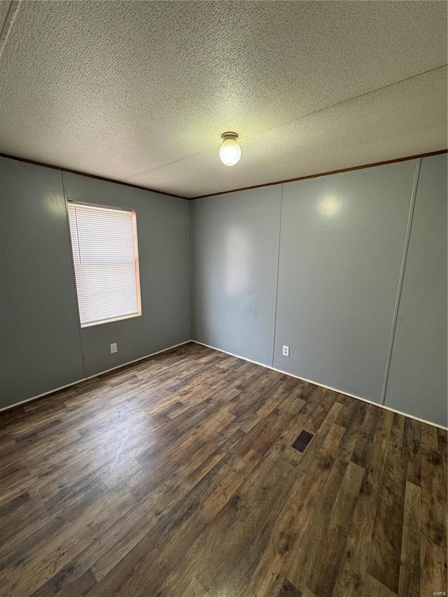 empty room featuring dark wood-type flooring, visible vents, and a textured ceiling