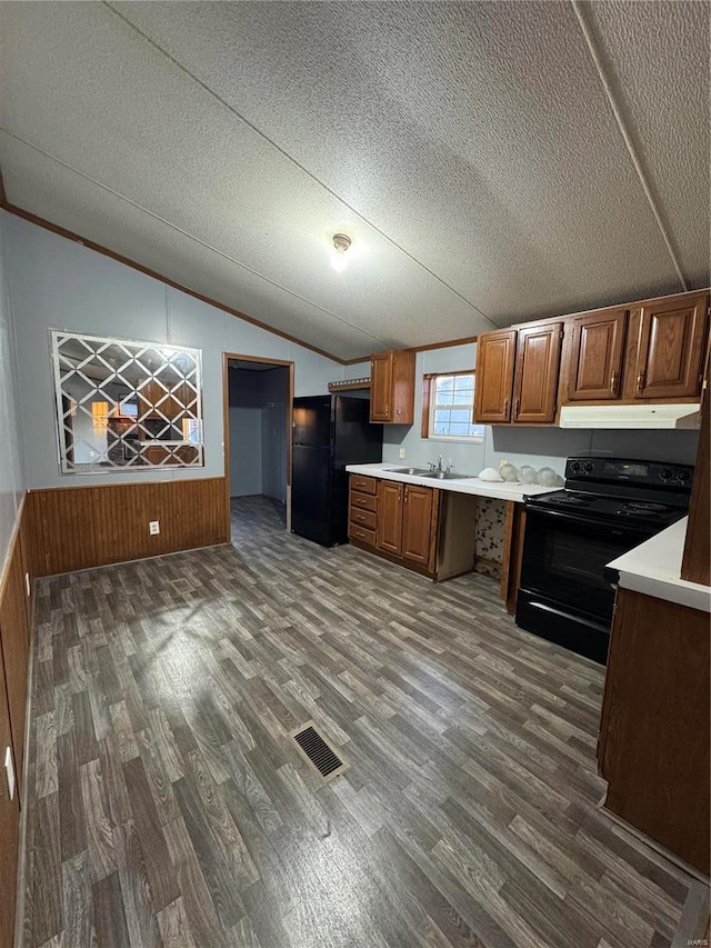 kitchen featuring under cabinet range hood, vaulted ceiling, light countertops, black appliances, and brown cabinetry