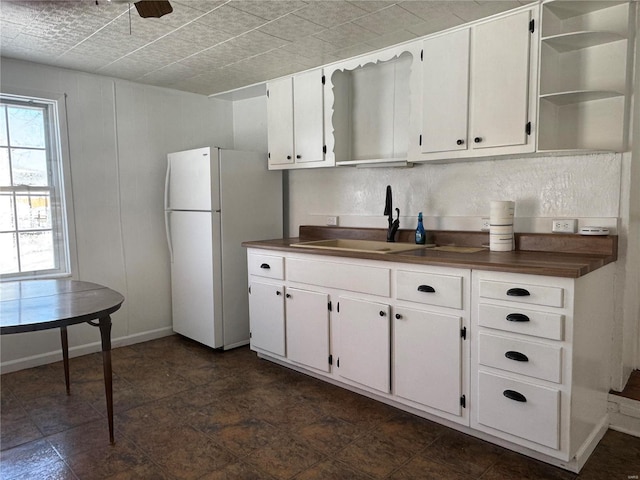 kitchen featuring open shelves, dark countertops, freestanding refrigerator, white cabinets, and a sink