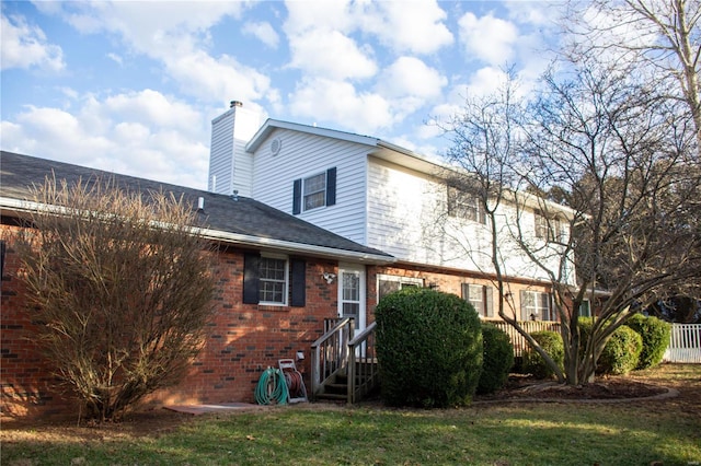 back of house featuring brick siding, a shingled roof, fence, a yard, and a chimney