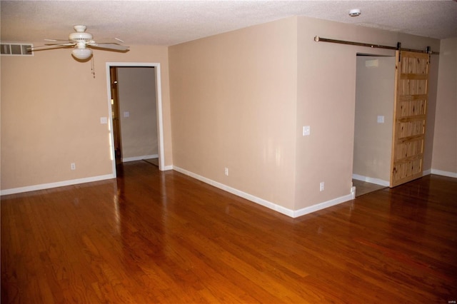 empty room featuring ceiling fan, a barn door, wood finished floors, visible vents, and baseboards