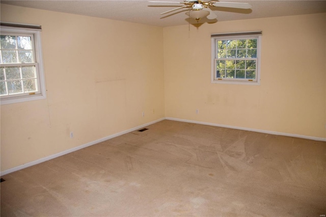 carpeted spare room featuring a ceiling fan, visible vents, and baseboards