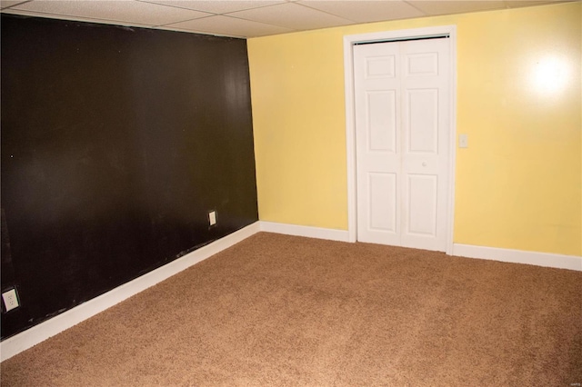 unfurnished bedroom with carpet floors, a closet, a drop ceiling, and baseboards