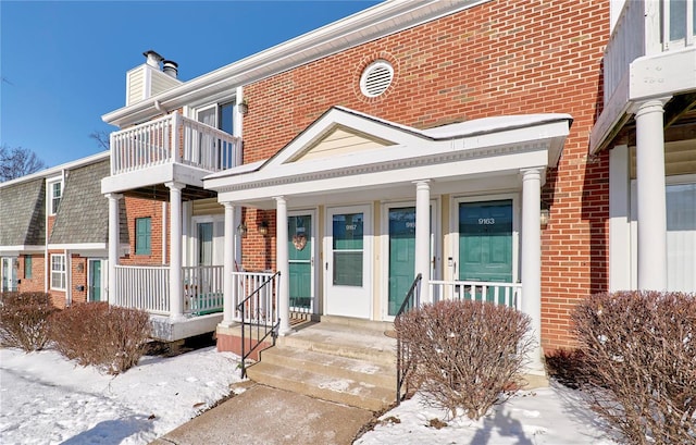 snow covered property entrance featuring covered porch and brick siding