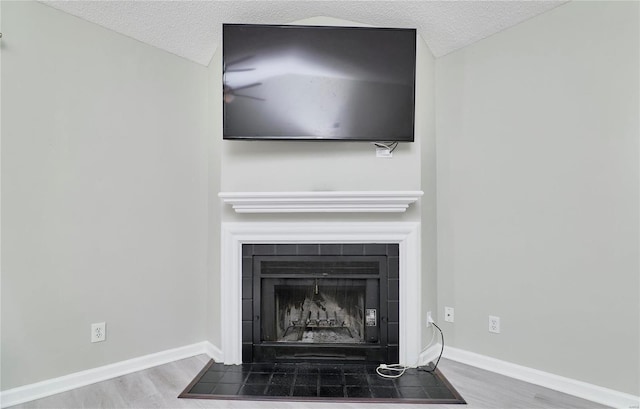 interior details featuring a fireplace with flush hearth, a textured ceiling, baseboards, and wood finished floors