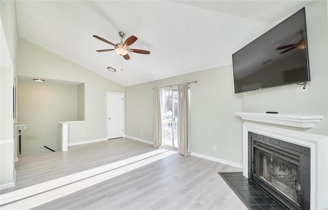 unfurnished living room featuring lofted ceiling, a tiled fireplace, a ceiling fan, wood finished floors, and baseboards