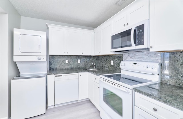 kitchen featuring white appliances, stacked washer and clothes dryer, and white cabinetry