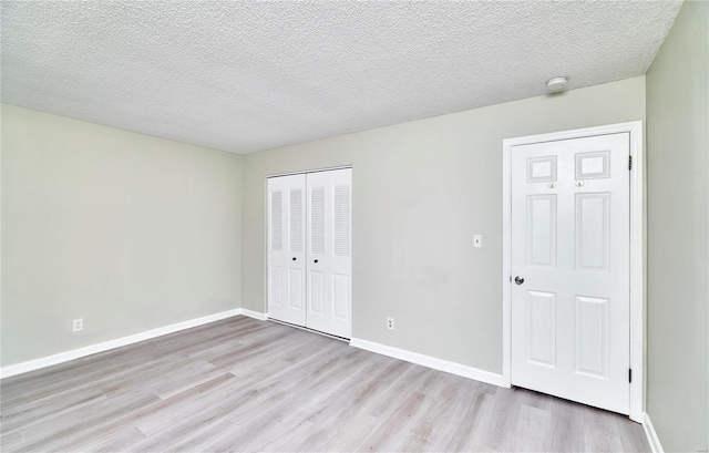 unfurnished bedroom with baseboards, a closet, a textured ceiling, and light wood-style floors