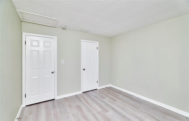 unfurnished bedroom featuring attic access, light wood-type flooring, a textured ceiling, and baseboards