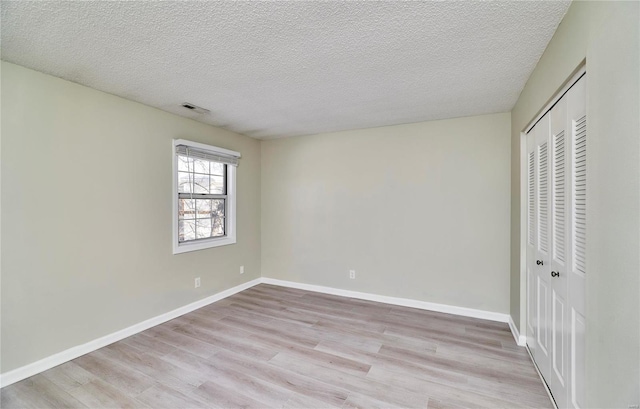 unfurnished bedroom with light wood-type flooring, a closet, a textured ceiling, and baseboards