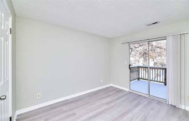 empty room featuring light wood finished floors, baseboards, visible vents, and a textured ceiling