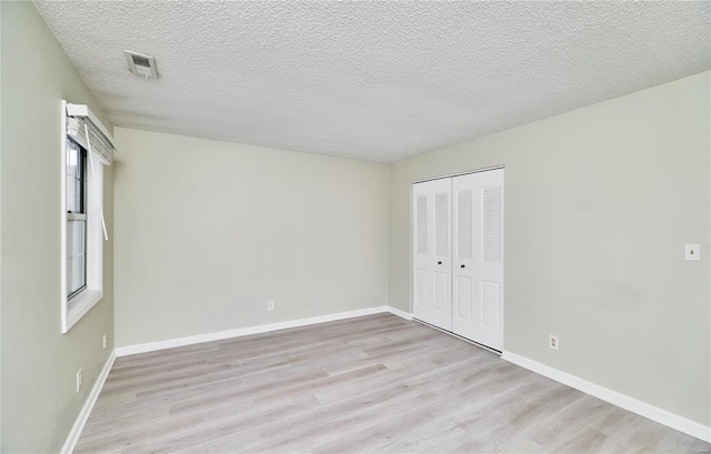 unfurnished bedroom with light wood-style floors, baseboards, visible vents, and a closet