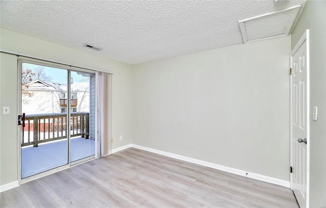 spare room with attic access, visible vents, baseboards, a textured ceiling, and light wood-type flooring