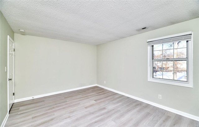 spare room featuring light wood-style flooring, a textured ceiling, visible vents, and baseboards