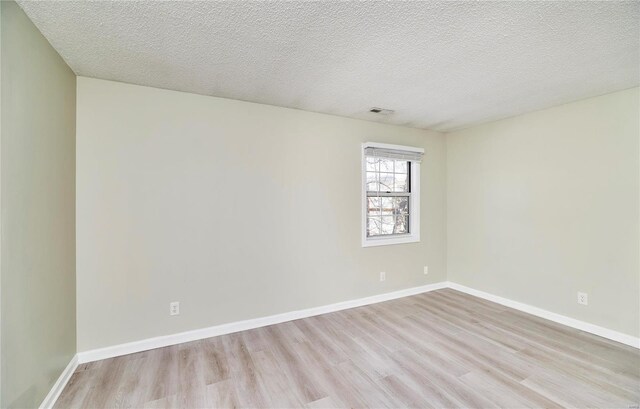 empty room featuring baseboards, a textured ceiling, visible vents, and light wood-style floors