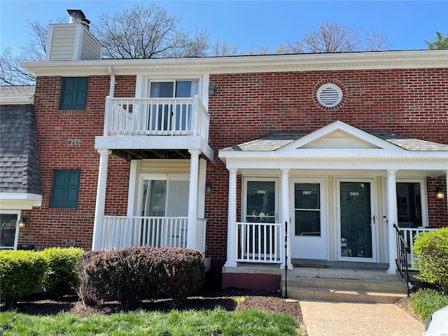 townhome / multi-family property with brick siding, a shingled roof, a chimney, and a balcony