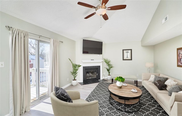 living room with a ceiling fan, visible vents, a fireplace with flush hearth, vaulted ceiling, and baseboards