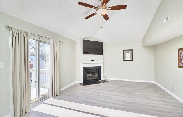 unfurnished living room featuring ceiling fan, visible vents, a fireplace with flush hearth, light wood finished floors, and lofted ceiling