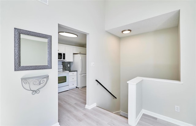 hallway with baseboards, visible vents, light wood finished floors, and an upstairs landing