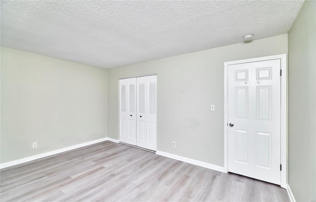 unfurnished bedroom featuring baseboards, a closet, light wood finished floors, and a textured ceiling