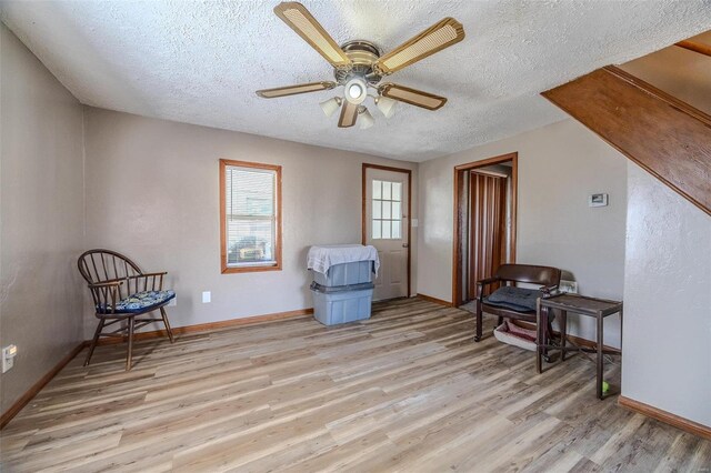 living area with a ceiling fan, light wood-type flooring, a textured ceiling, and baseboards