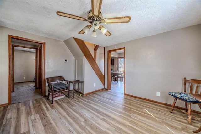 living area with a textured ceiling, baseboards, a ceiling fan, and light wood-style floors