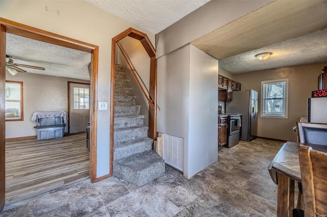 staircase with ceiling fan, a textured ceiling, visible vents, and a wealth of natural light