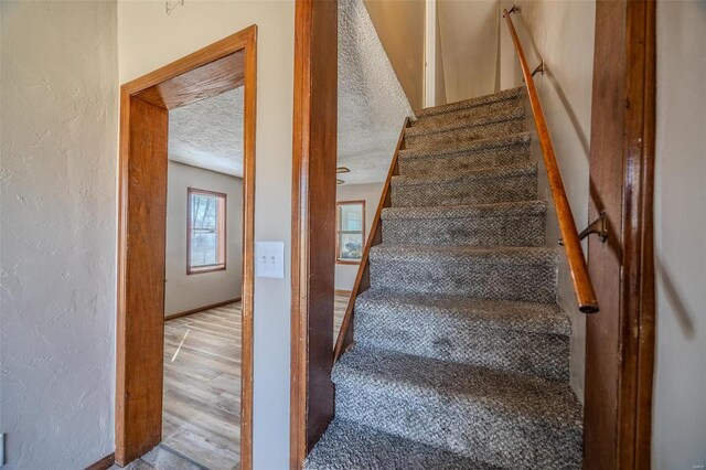 stairs with a textured wall, a textured ceiling, baseboards, and wood finished floors