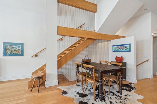 dining space featuring visible vents, baseboards, wood finished floors, and a towering ceiling