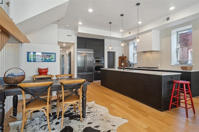 kitchen featuring visible vents, a center island with sink, light countertops, custom exhaust hood, and stainless steel appliances