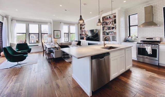 kitchen with dark wood-style floors, appliances with stainless steel finishes, open floor plan, a sink, and wall chimney exhaust hood