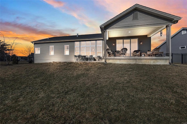 back of property at dusk with fence, a patio, and a yard