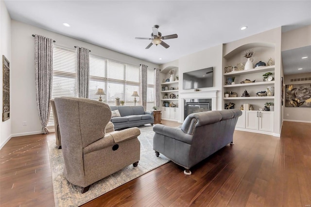 living room with built in features, a glass covered fireplace, dark wood-style flooring, and baseboards