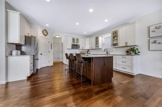 kitchen featuring dark wood-style floors, stainless steel appliances, glass insert cabinets, and a kitchen breakfast bar