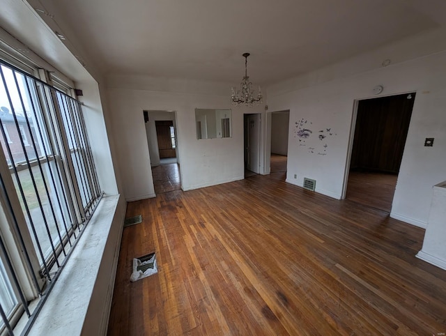 spare room with a healthy amount of sunlight, visible vents, a notable chandelier, and wood finished floors