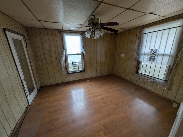 spare room with a paneled ceiling, wood walls, and light wood-style flooring