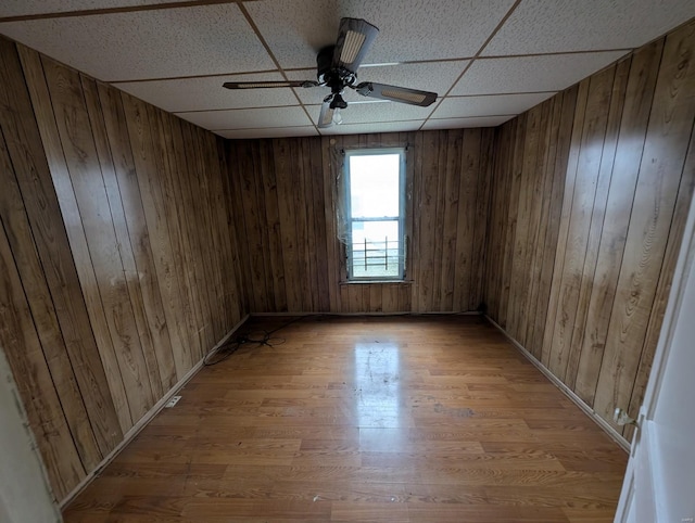 empty room with ceiling fan, wood walls, a drop ceiling, and light wood-style floors