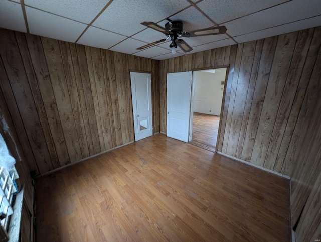 unfurnished bedroom with wood walls, baseboards, a drop ceiling, and wood finished floors