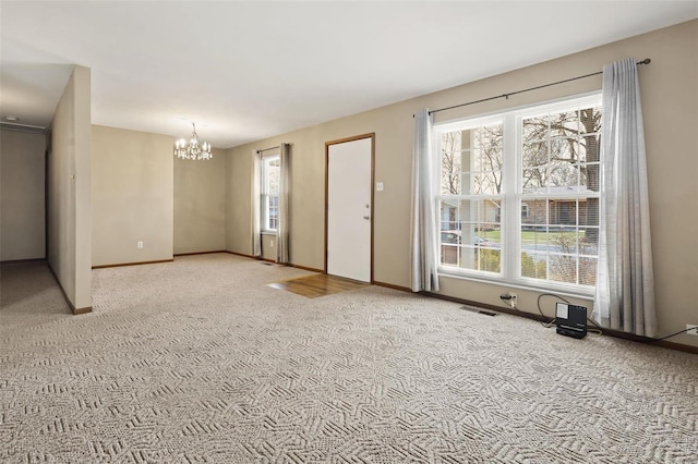 spare room with light carpet, a notable chandelier, baseboards, and visible vents